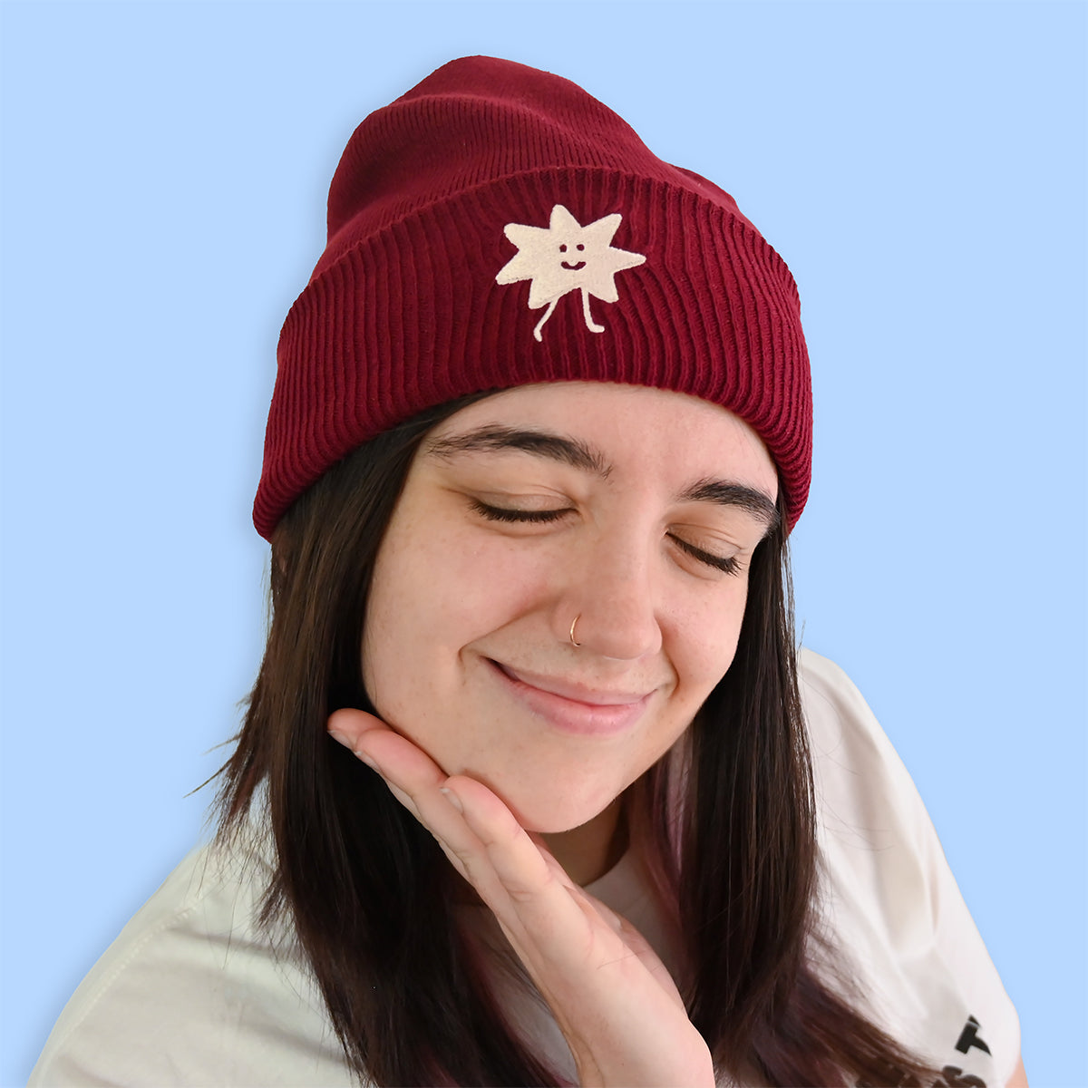 Person wearing a plum beanie with a smiley face design on a light blue background