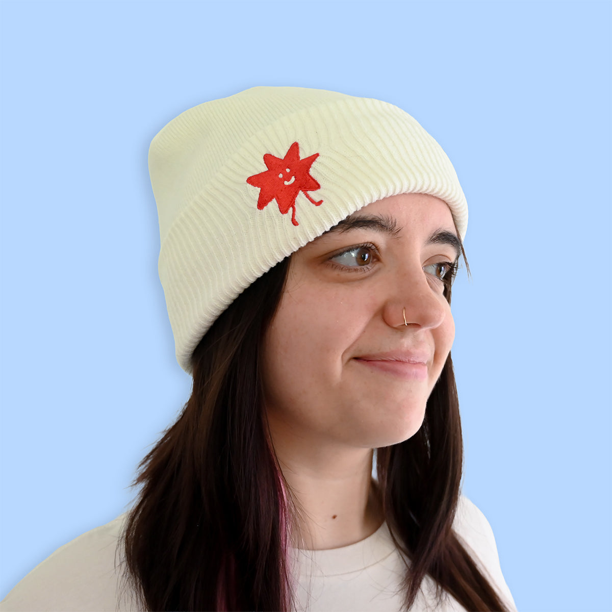 Person wearing a cream beanie with a smiling design on a light blue background