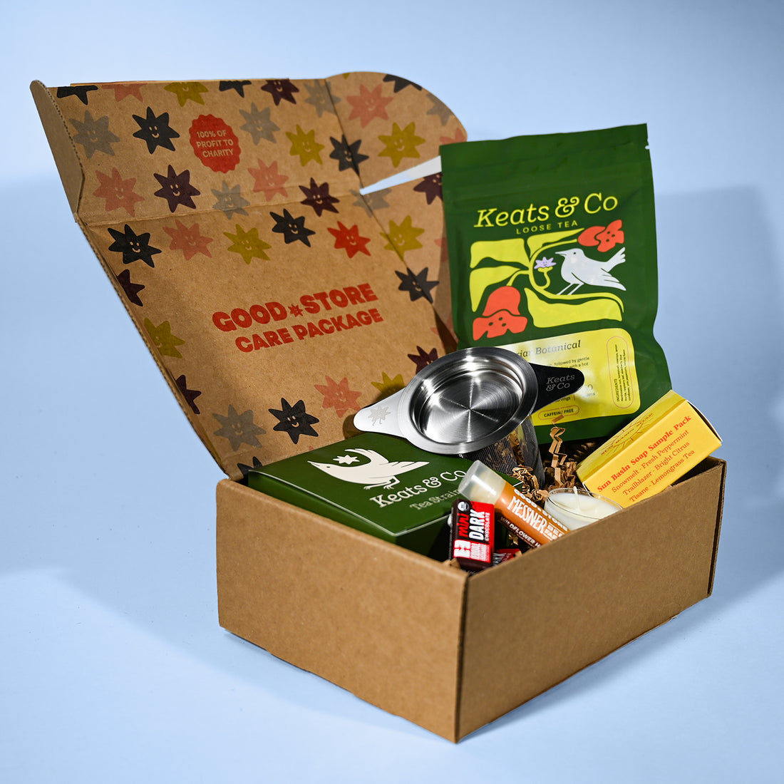 Open cardboard care package with tea packaging and a strainer on a light blue background