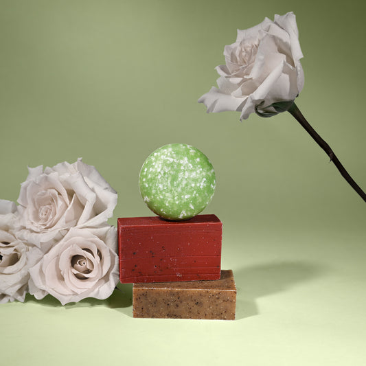 Green shampoo bar on two soap bars with white roses on a light green background