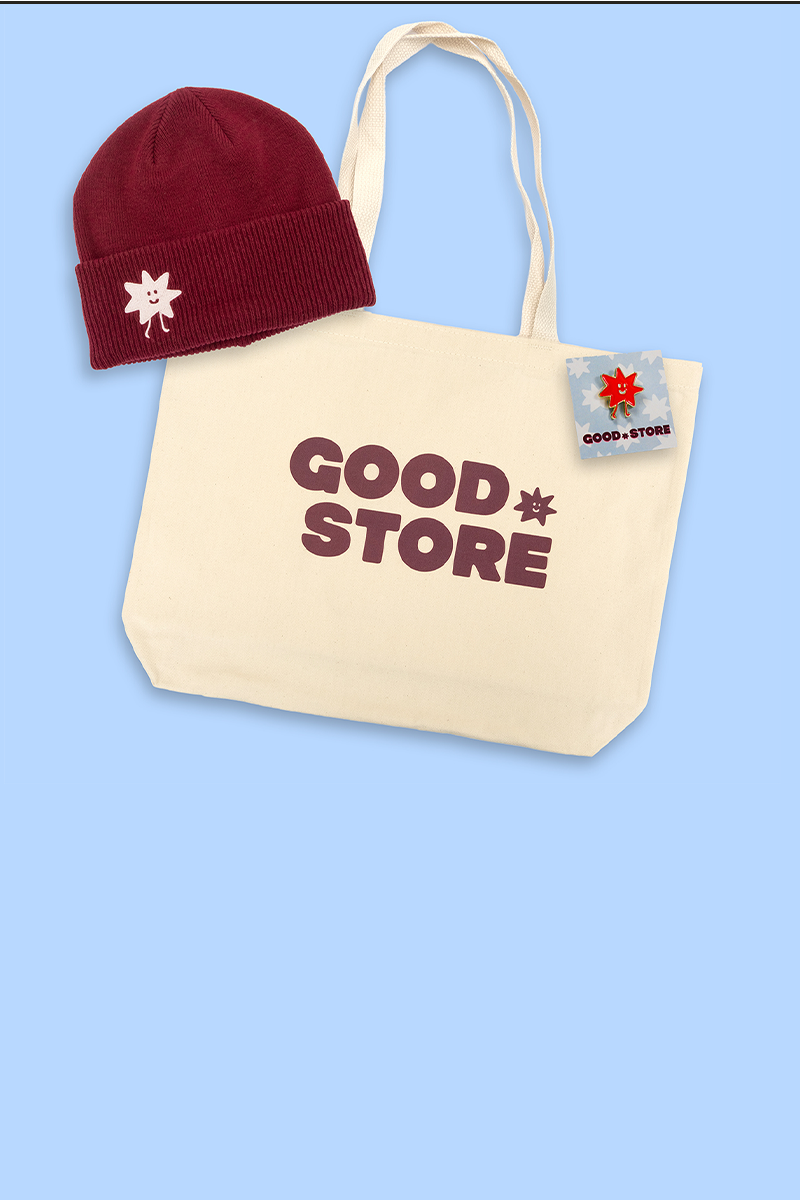 Beige tote bag with 'GOOD STORE' text, red beanie with white flower design, and small card on a light blue background