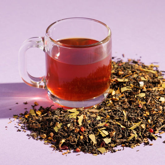 Glass cup of redish Golden Moon tea positioned next to a pile of loose leaf tea blend containing on a purple background. A Good Store product.