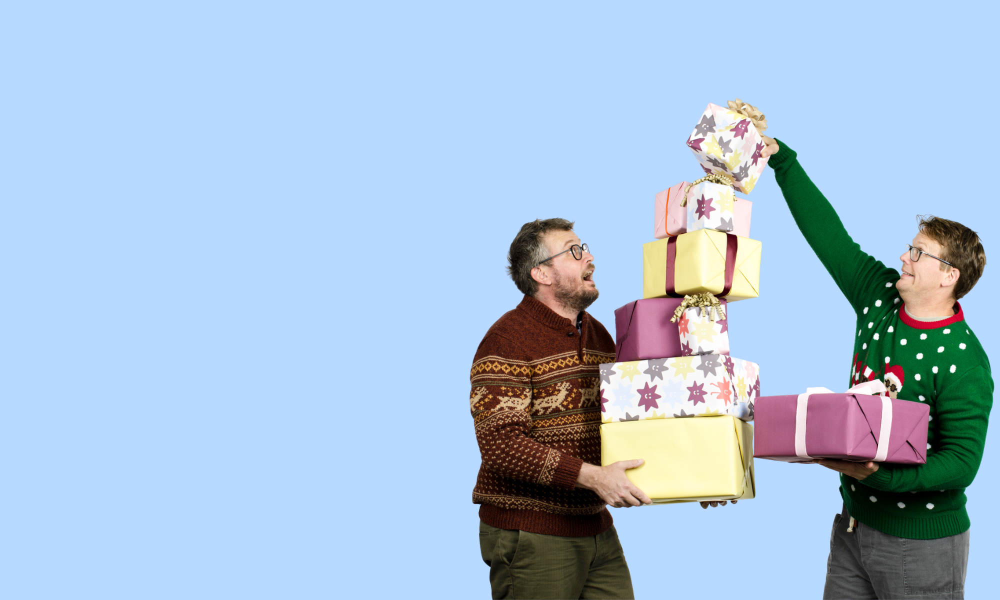 Hank and John Green holding a stack of colorful gifts against a blue background