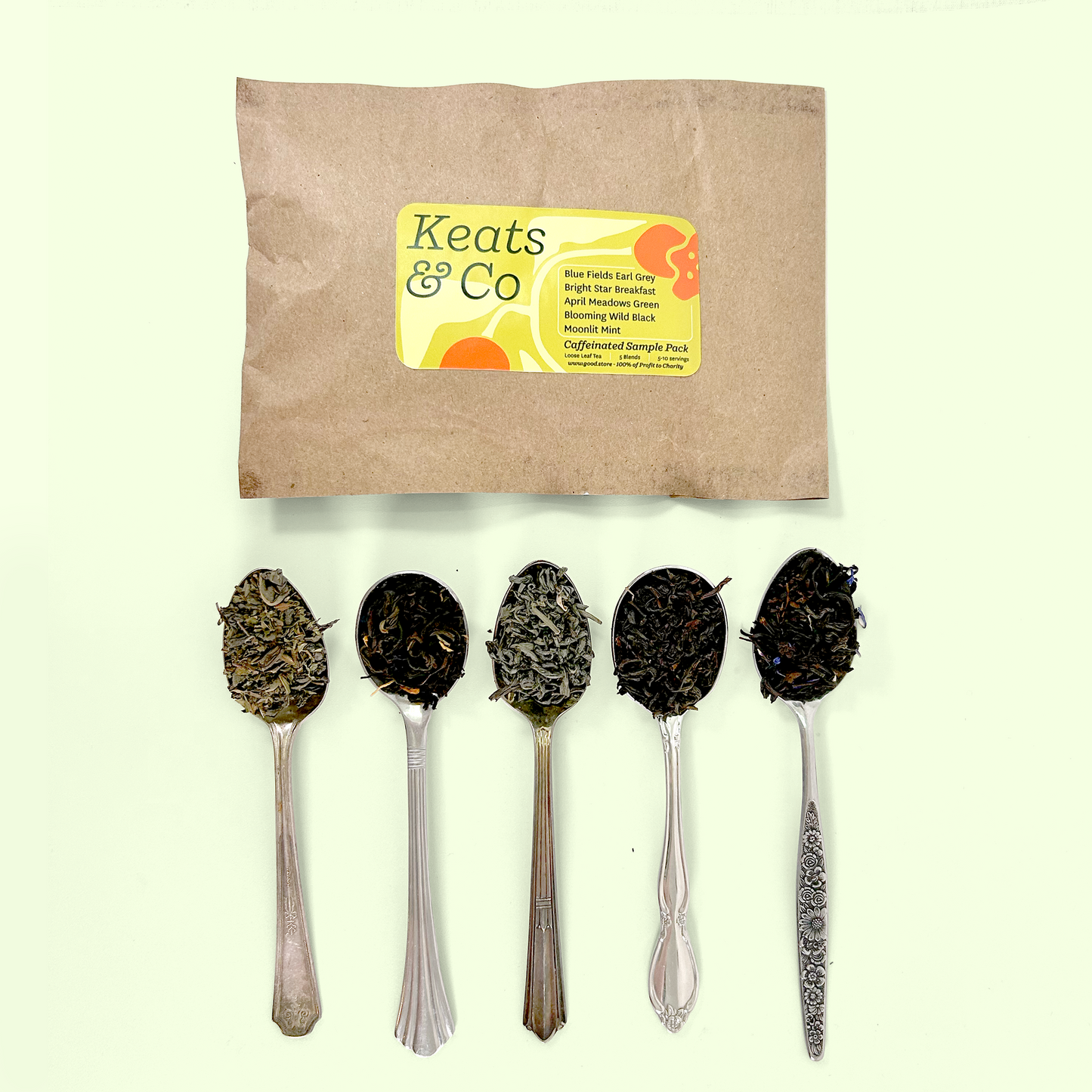 A Keats & Co tea sample pack in brown kraft paper packaging with a yellow label reading 'Caffeinated Sample Pack' listing varieties including Blue Fields Earl Grey, Bright Star Breakfast, April Meadows Green, Blooming Wild Black, and Moonlit Mint. Below the package are five silver spoons containing the corresponding tea samples, showing the variety from light green teas to dark black teas.