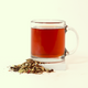  A clear glass mug filled with reddish-brown tea - Evensong Chai -  next to a small pile of dried tea leaves. A Good Store product.