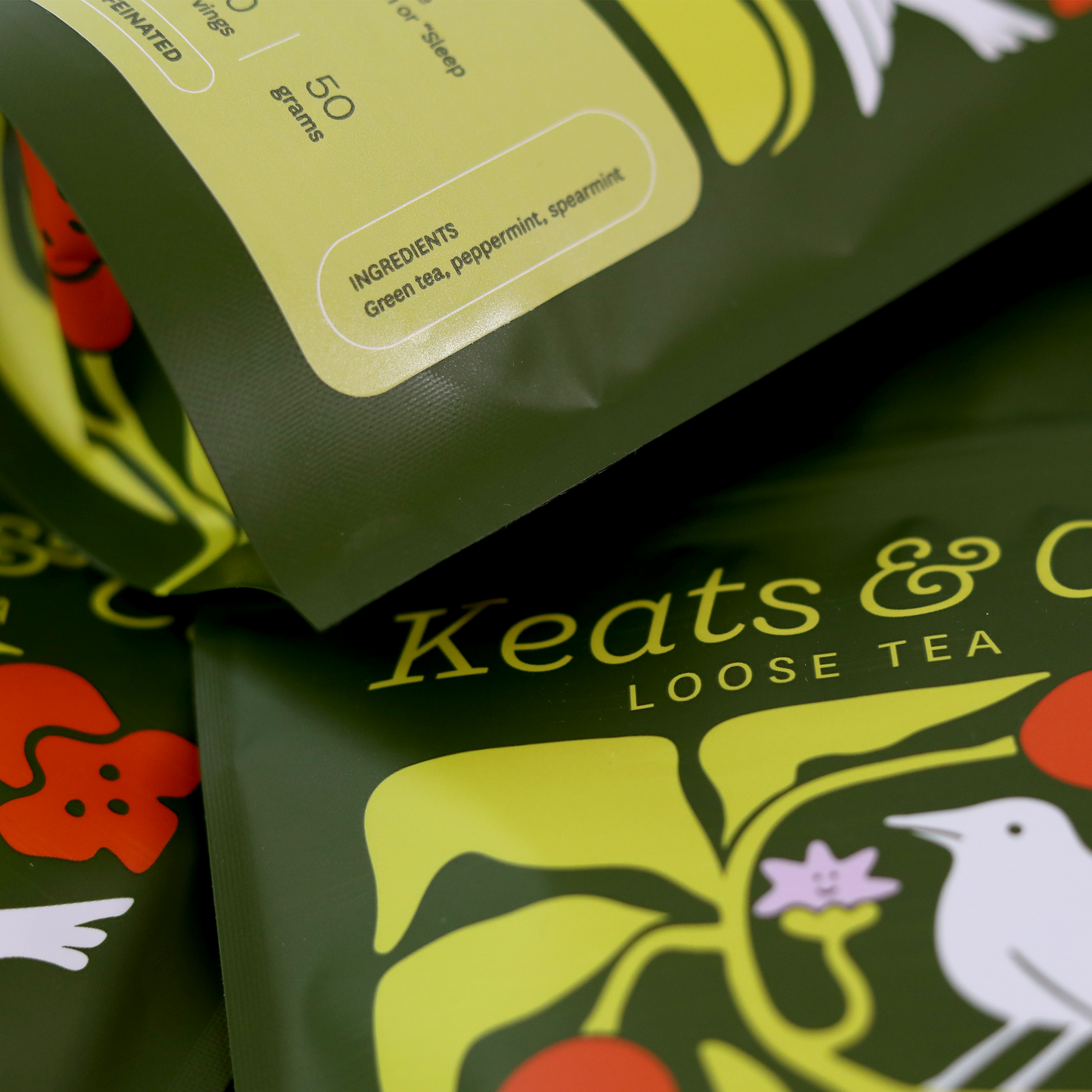 A close up of green and white tea packaging bags featuring an illustrated Nightingale logo and red floral accents are arranged to display the front and back labels. The bags contain loose leaf tea blends from Keats & Co. The front labels show the tea variety names, while the back labels provide additional product details and brewing instructions. A Good Store product.