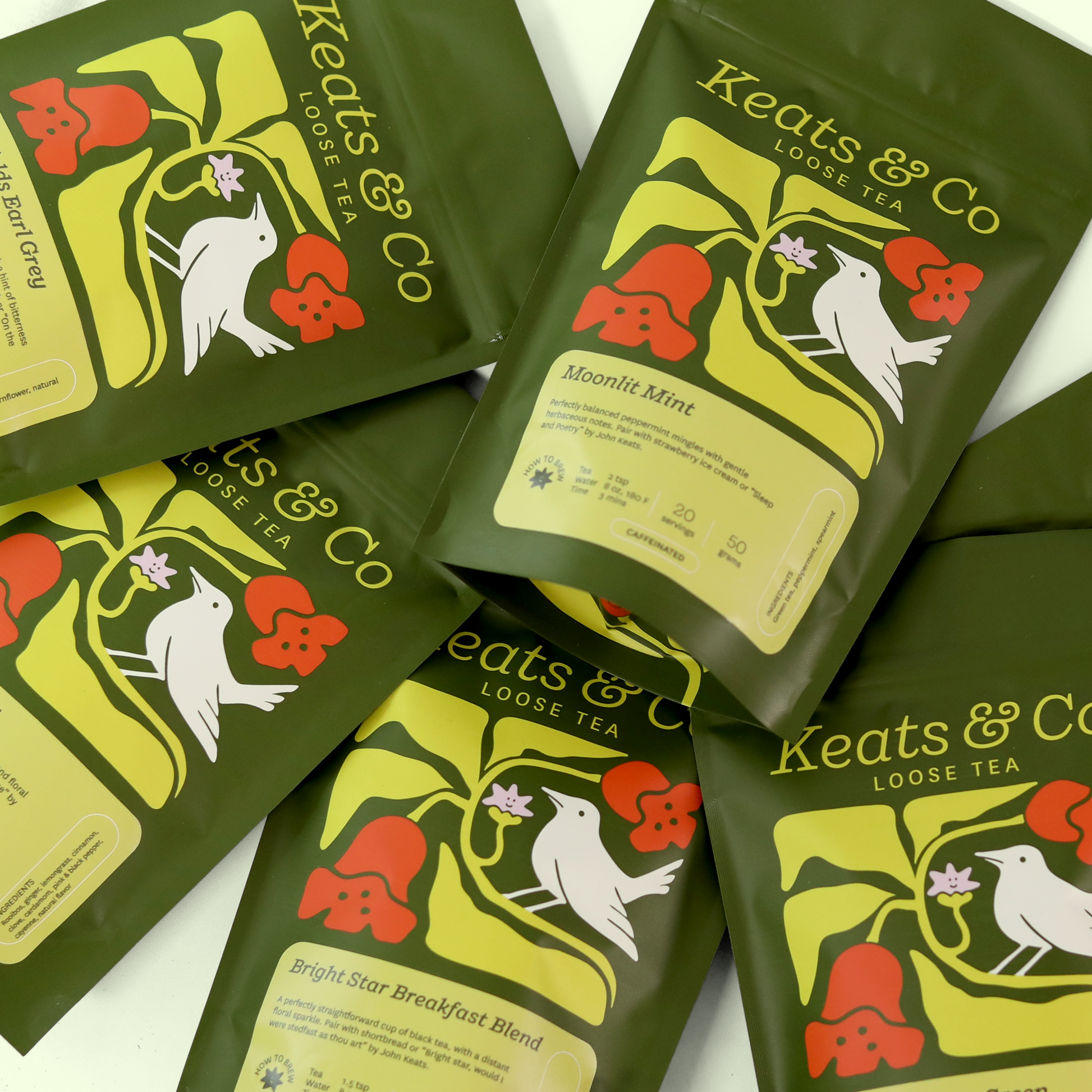 Several green and white tea packaging bags featuring an illustrated Nightingale logo and red floral accents are arranged to display the front and back labels. The bags contain loose leaf tea blends from Keats & Co. The front labels show the tea variety names, while the back labels provide additional product details and brewing instructions. A Good Store product.