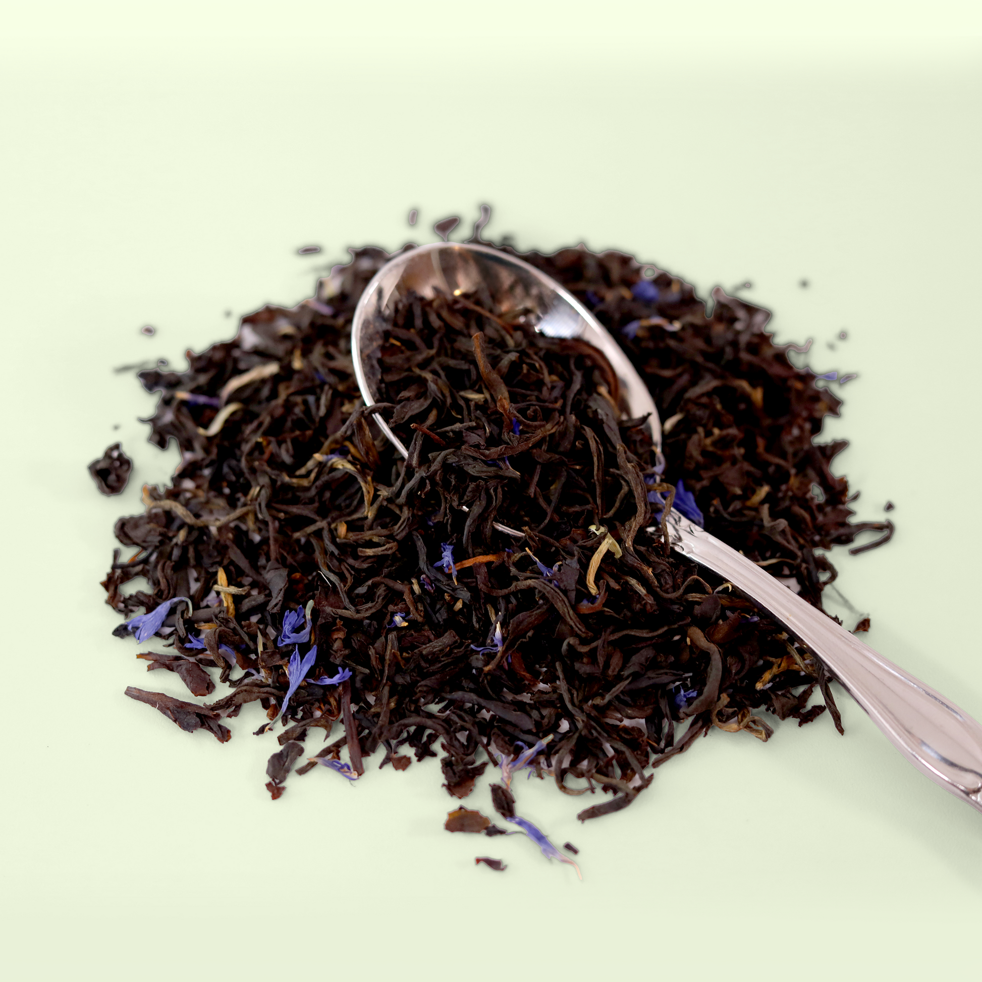  A close-up view of a pile of dried Blue Fields Earl Grey tea leaves. A metal spoon is visible, scooping up some of the tea blend. A Good Store product.