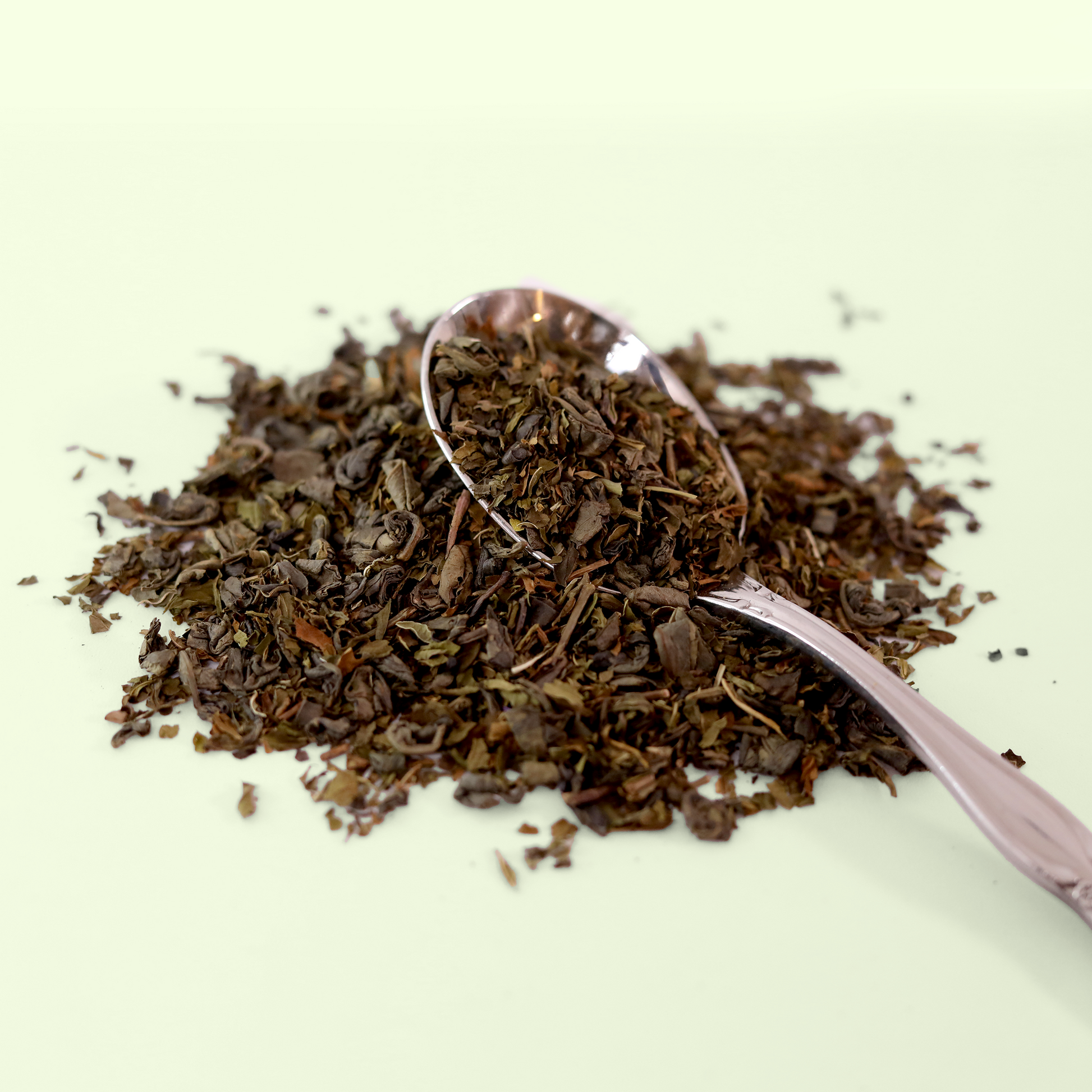 A close-up view of a pile of dried Moonlit Mint tea leaves. A metal spoon is visible, scooping up some of the tea blend. A Good Store product.