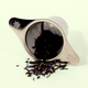 A metal loose-leaf tea strainer is laid on its side with  tea leaves spilling out. The handles of the strainer have a Dot engraving and "Keats & Co". A Good Store product.