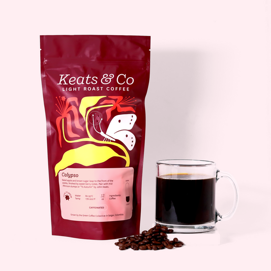 A burgundy-colored coffee bag labeled "Keats & Co Dark Roast Coffee-Calypso" with colorful floral and butterfly designs. Next to the bag is a clear glass mug filled with dark coffee and a few coffee beans scattered around. The items are placed on a white surface against a light pink background. A Good Store product.