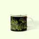 A detailed view of the Keats & Co Meadow glass mug. It's filled with coffee and the mug's design shows green illustrations of plants, flowers, and a bird, along with the Keats & Co logo. A Good Store product. 