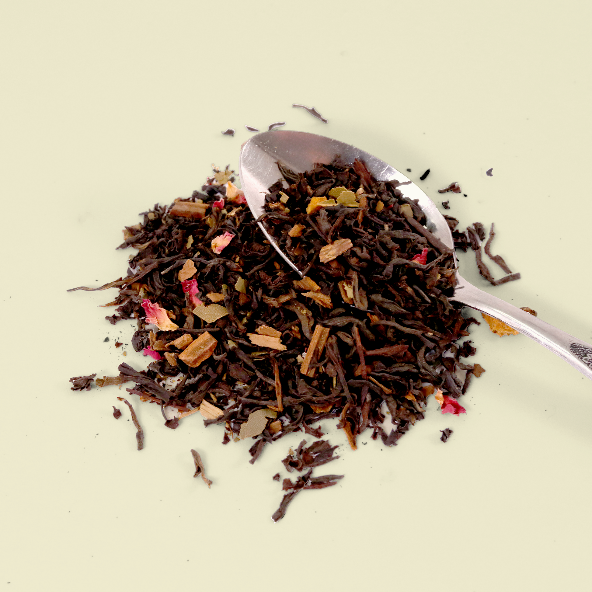 A pile of loose leaf tea on a light background. The tea appears to be a black tea blend with visible pieces of dried fruit or flower petals mixed in. A small silver spoon is partially visible in the tea pile. Keats & Co. 