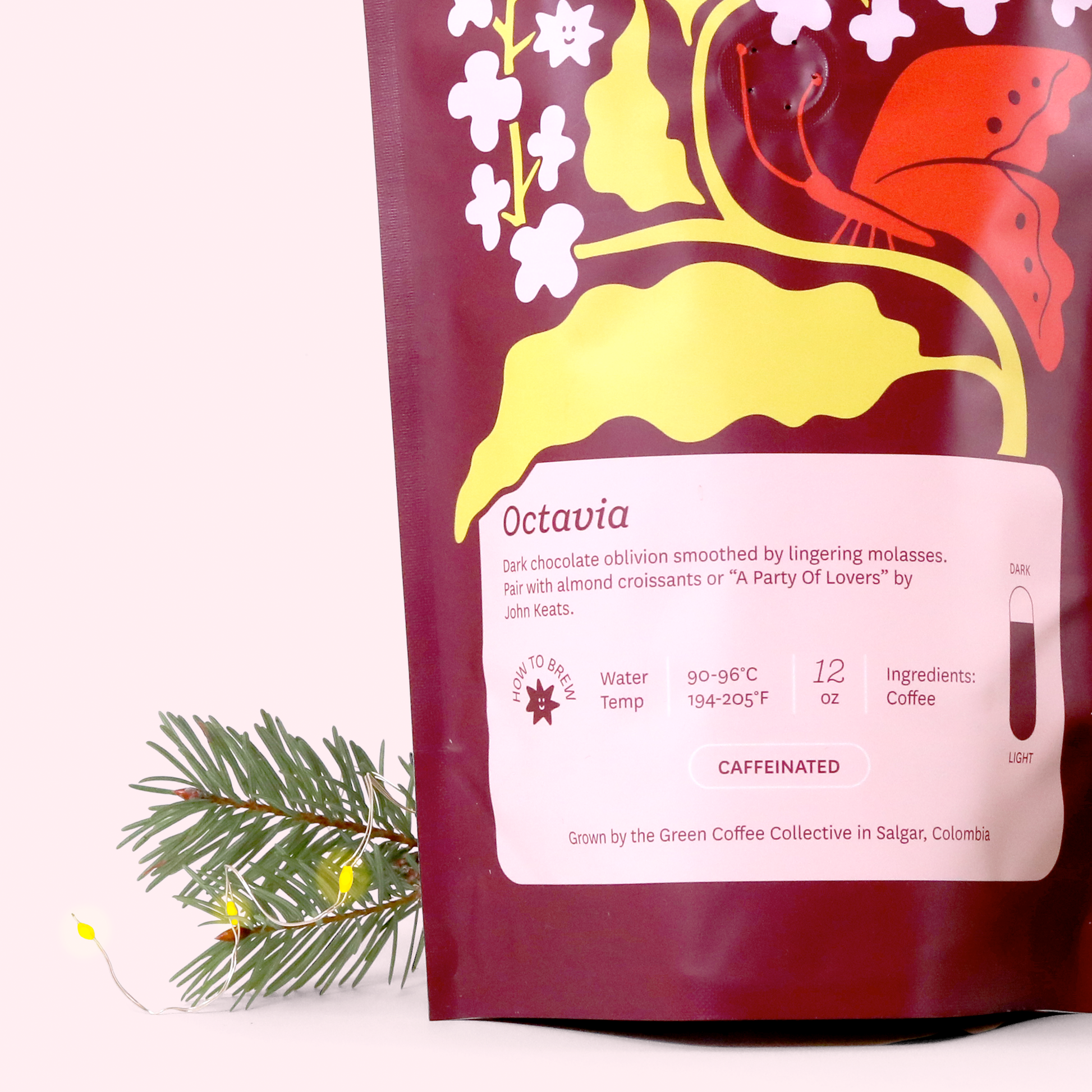 A close-up of a burgundy coffee bag labeled 'Octavia' from Keats & Co, featuring decorative yellow branches, white flowers, and an orange butterfly. The label includes brewing instructions and notes it was grown in Salgar, Colombia. A pine branch is visible in the corner.