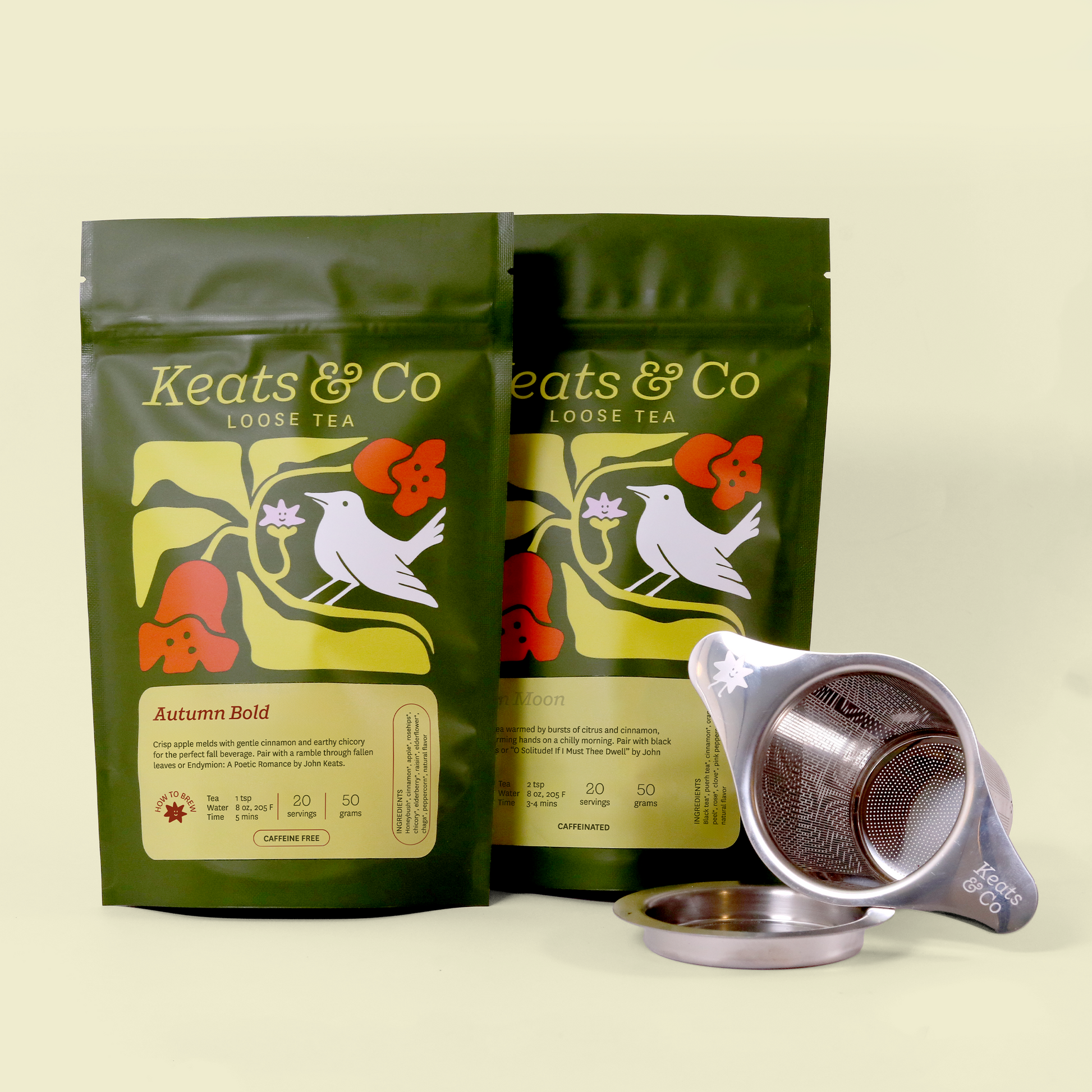  Two green packages of Keats & Co loose tea with a decorative bird and flower design on the packaging. The front package shows "Autumn Bold" variety and the back shows "Golden Moon". A metal tea strainer with the Keats & Co logo is placed beside the packages.