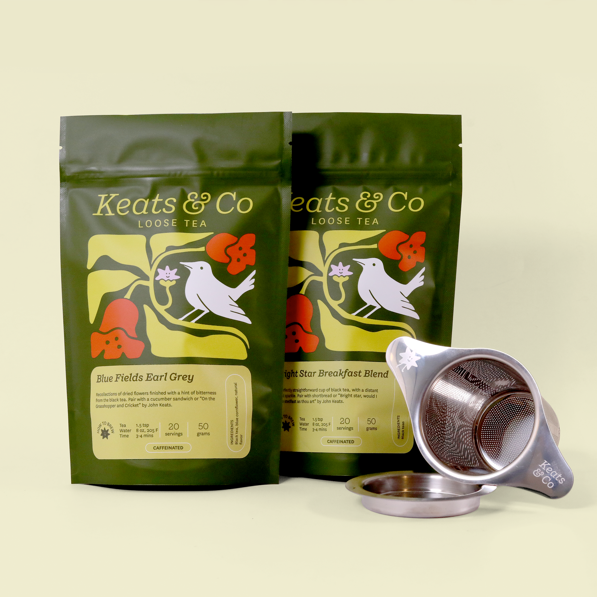 Product photo of two green Keats & Co loose tea packages featuring a white bird and floral design, displayed with a silver tea strainer and its base. The packages show "Blue Fields Earl Grey" and "Bright Star Breakfast Blend" varieties against a cream-colored background. The packaging includes brewing instructions and serving information.