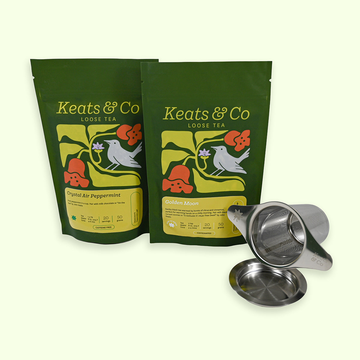 Two green tea packages with floral designs and a metal tea infuser on a white background