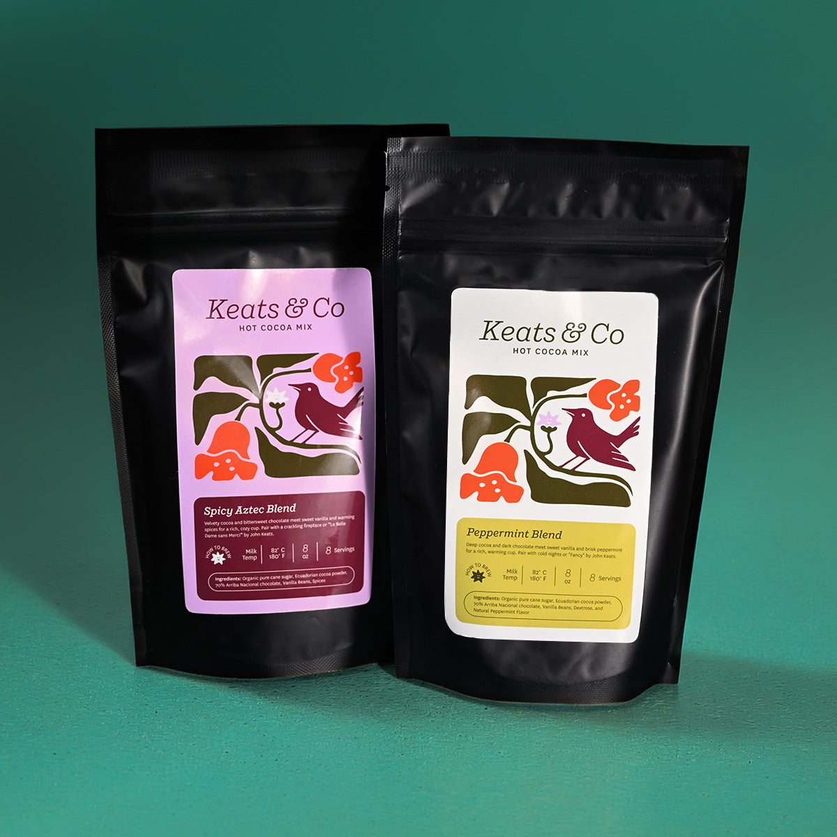 Two stand-up pouches of Keats & Co hot cocoa mix on a teal background. The left pouch is black with a lavender and burgundy label reading Spicy Asterix Blend.