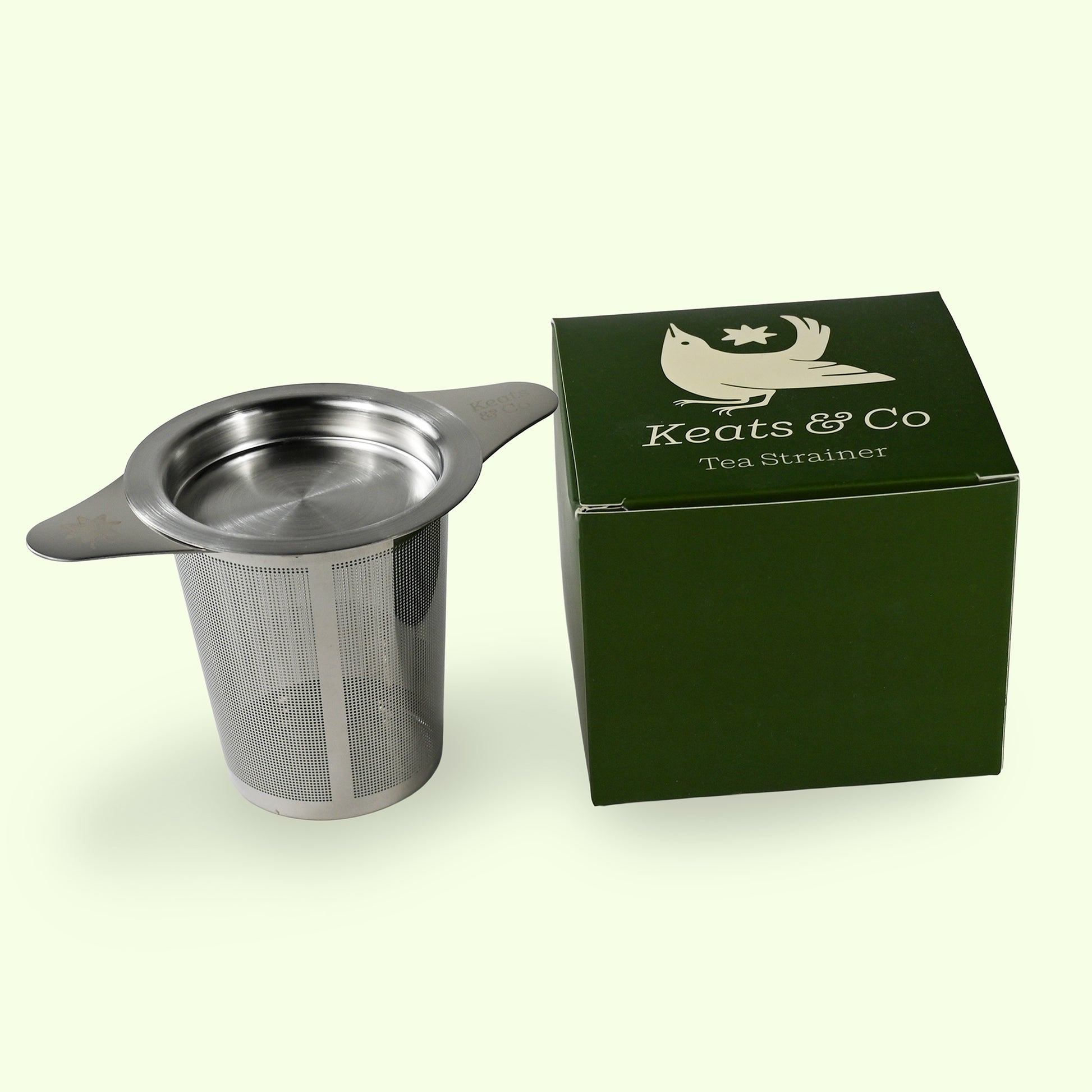 Metal tea strainer with green box labeled 'Keats & Co' on a white background
