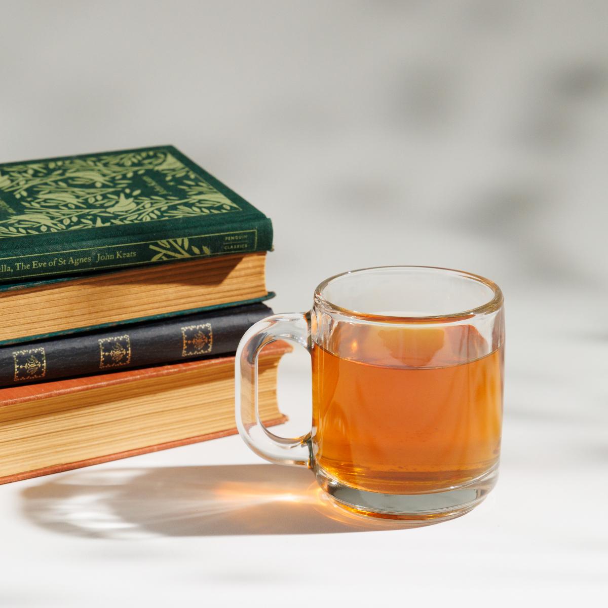 Cup of yellowish Keats & Co Loose Leaf Thrushsong Oolong tea in a glass cup next to a pile of John Keats books on a white background. 