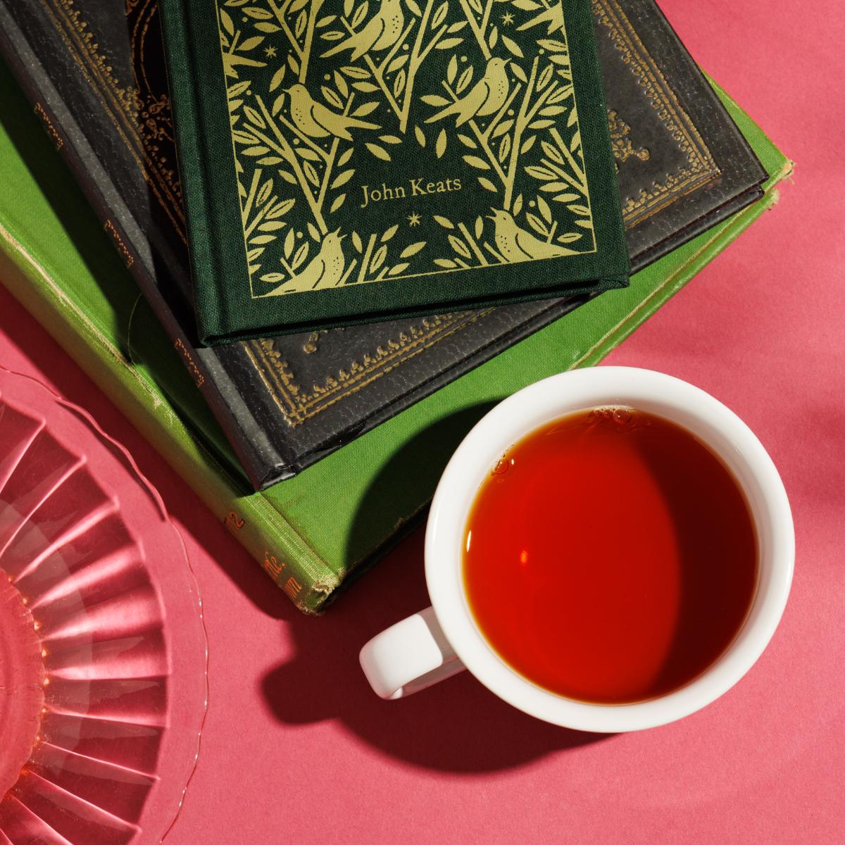 Overhead shot of tea in a white mug next to a pile of John Keats books. 