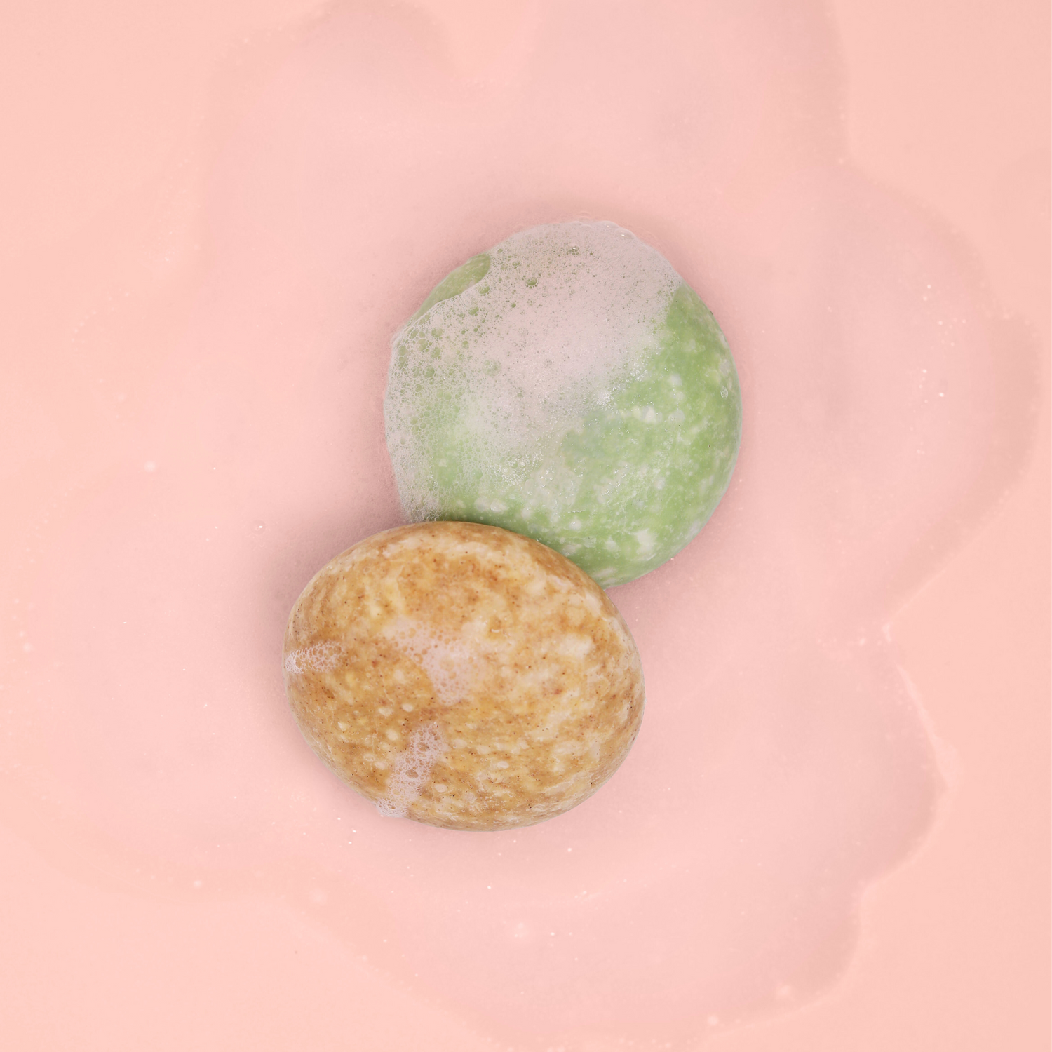 The Dew Drop and Bloom Shampoo bars covered in soap on a pink background.