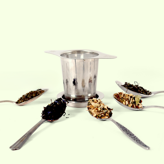 A stainless steel mesh tea infuser in the center surrounded by five silver spoons in a circular arrangement, each containing different loose tea blends ranging from dark black tea to lighter herbal mixtures with visible dried flowers and fruits.