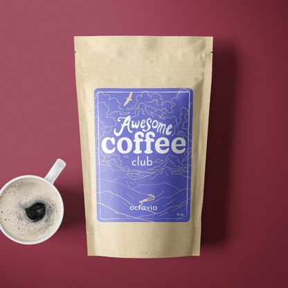 A photo of a brown bag of coffee with a light purple label that shows a mountain scene and has the text "Awesome Coffee Club; Octavia". The bag sites atop a maroon background with a cup of coffee next to it
