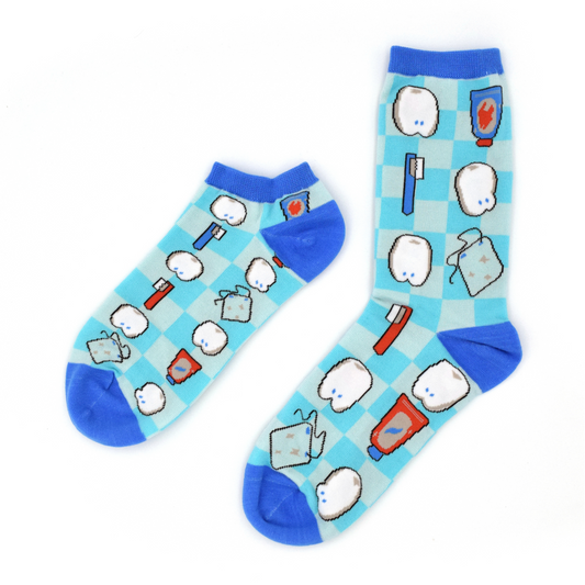 Two past designs from the Awesome Socks Club, one ankle, one crew, with a light blue checkered background and mini teeth, floss, toothbrush and toothpaste. A Good Store product.