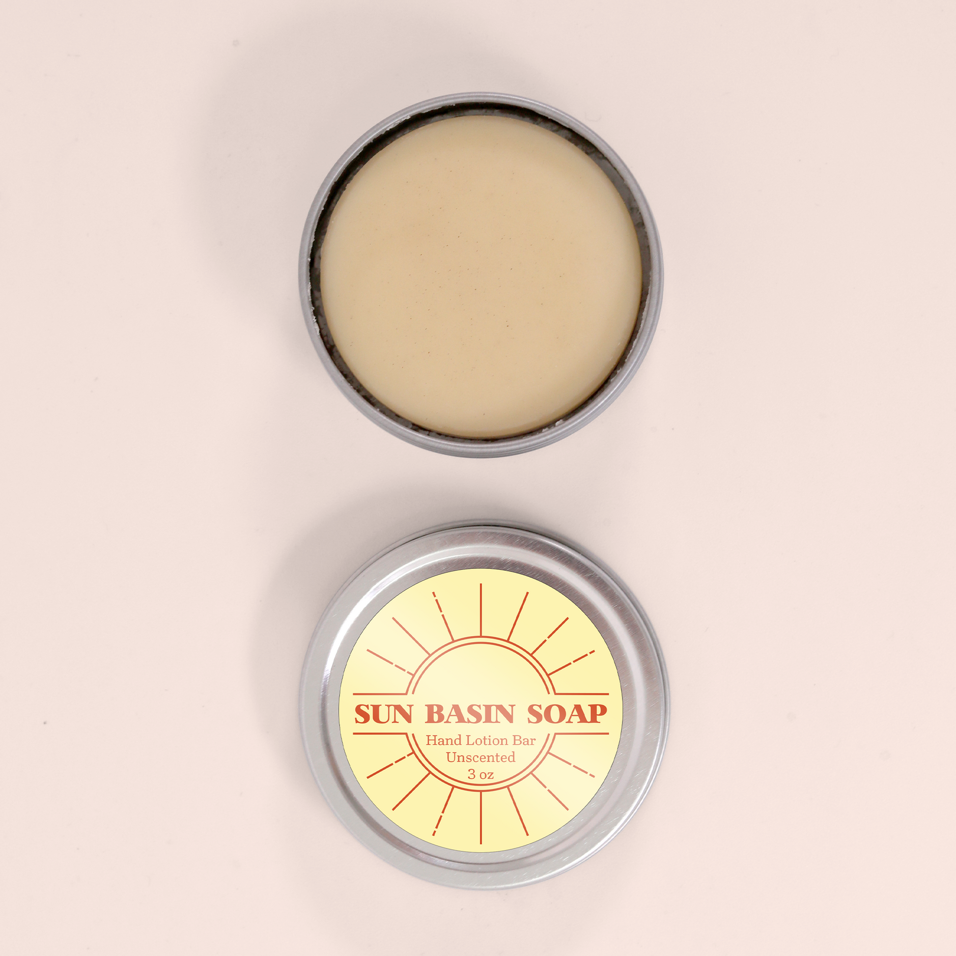 Two round silver metal tins against a light pink background - the top tin shows cream-colored lotion bar product inside, while the bottom tin displays its yellow label with red sun logo reading "SUN BASIN SOAP Hand Lotion Bar Unscented 3 oz."