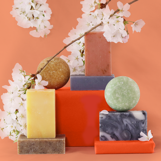 Sun Basin Soap bars and circular shampoo bars rest on top of each other with cherry blossoms in the background.  