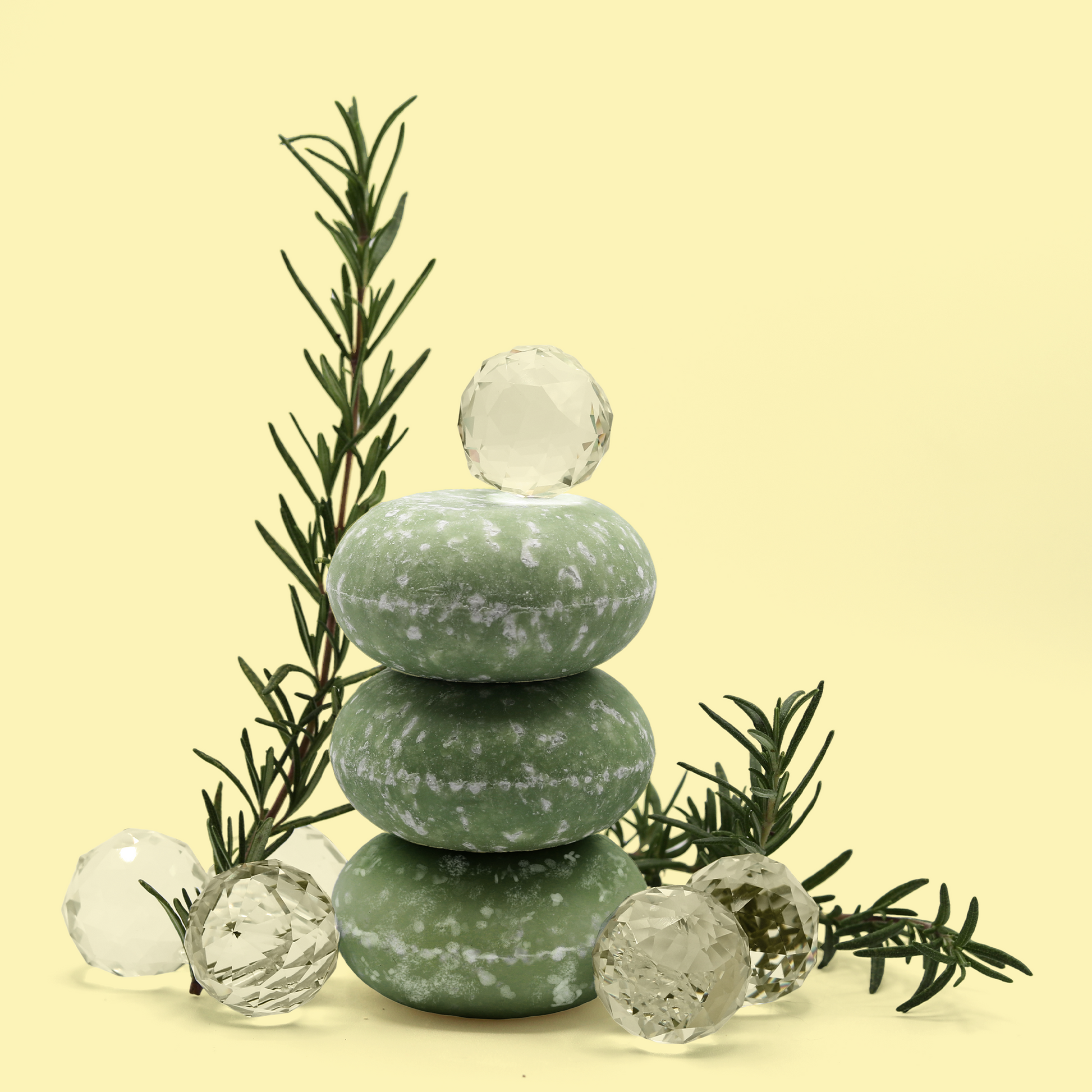 Three bars of the Dew Drop shampoo bars from Sun Basin Soap are stacked on top of each other. The bars are surrounded by shiny crystal balls and sprigs of rosemary. A Good Store subscription product.