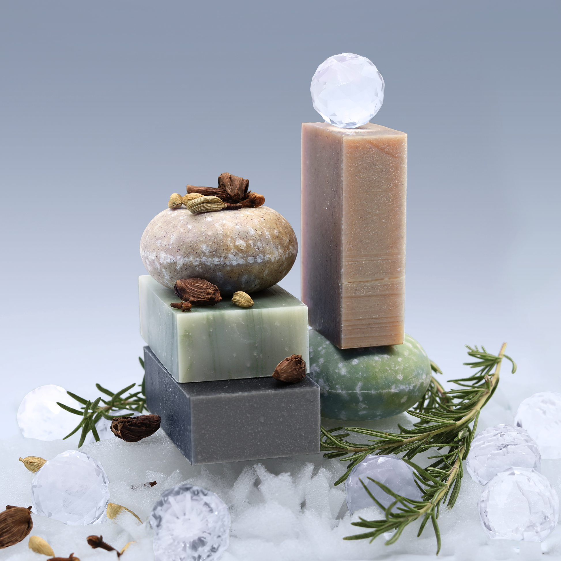 Three bars of the Sun Basin Soap holiday scents are piled up with the two shampoo cars atop rosemary springs, snow, glass balls and cardamon. A Good Store product. 