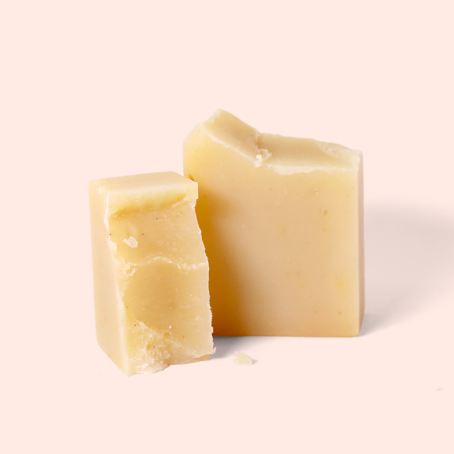 A pale yellow soap blocks broken in half on a light pink background. Both have a smooth texture with slight imperfections on cut edges. Sun Basin Soap - Good Store. 