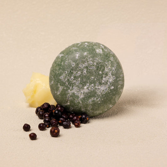 A round green shampoo bar styled with dark berries on a neutral beige background.