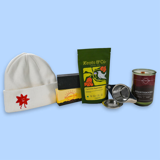 Collection of items including a cream beanie, tea packaging, and a candle on a light blue background