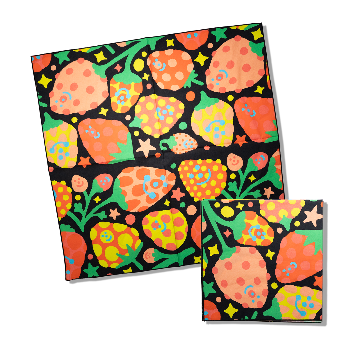 A square black fabric bandana featuring a vibrant, hand-drawn style pattern of strawberries, stars, and leaves in orange, green, yellow, and blue. A second folded version of the same patterned fabric is shown in the lower right corner against a clean white background.